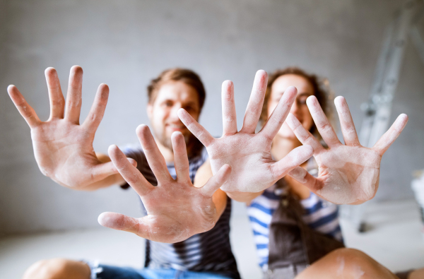 Beautiful young couple painting walls in their new house, sitting on the floor. Close up of their hands. Home makeover and renovation concept.