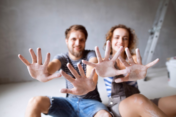 Beautiful young couple painting walls in their new house, sitting on the floor. Close up of their hands. Home makeover and renovation concept.