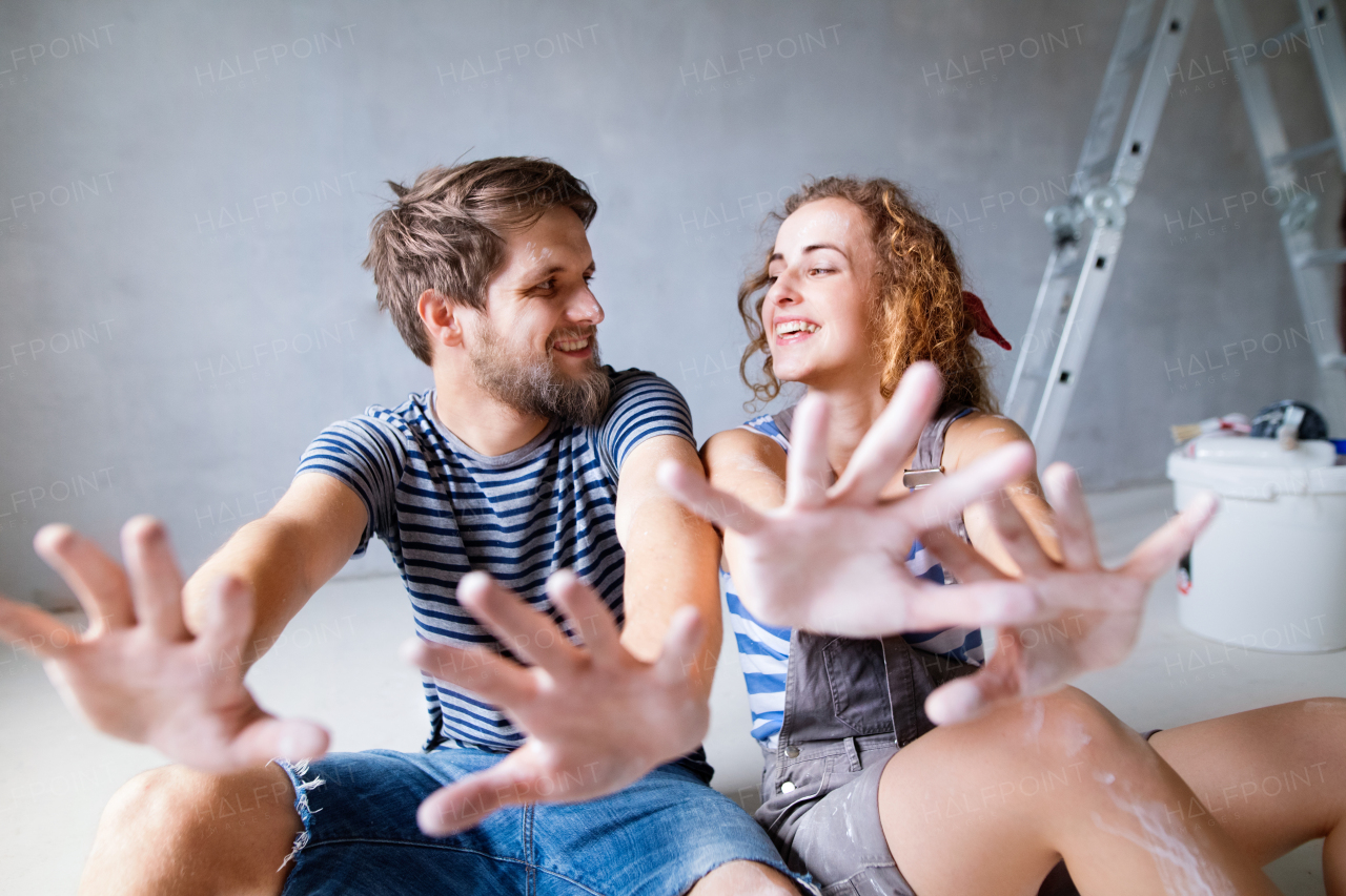 Beautiful young couple painting walls in their new house, sitting on the floor. Close up of their hands. Home makeover and renovation concept.