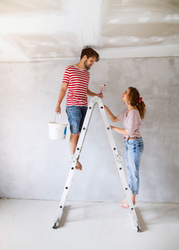 Beautiful young couple painting walls in their new house using paint brushes. Home makeover and renovation concept.