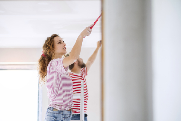 Beautiful young couple painting walls in their new house using paint brushes. Home makeover and renovation concept.