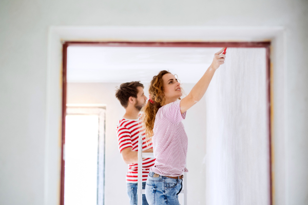 Beautiful young couple painting walls in their new house using paint brushes. Home makeover and renovation concept.