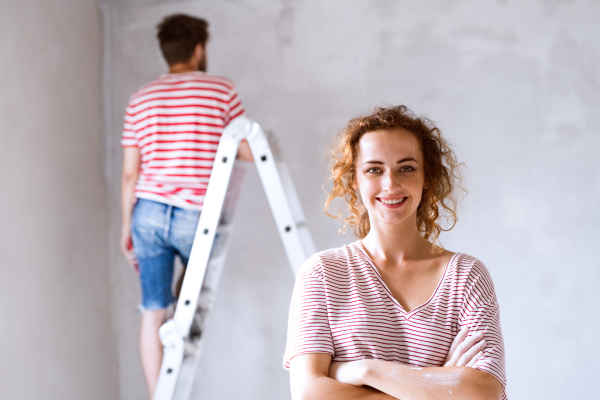 Beautiful young couple painting walls in their new house using paint brushes. Home makeover and renovation concept.