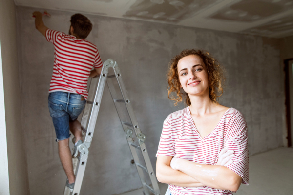 Beautiful young couple painting walls in their new house using paint brushes. Home makeover and renovation concept.