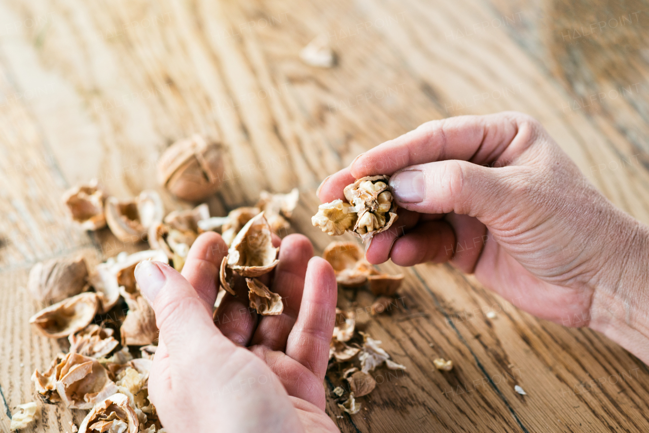 Hands of unrecognizable woman cracking walnuts, taking them out of shell, wooden table.