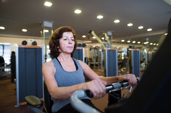 Beautiful fit senior woman in sports clothing in gym doing cardio workout, exercising on recumbent bicycle. Sport fitness and healthy lifestyle concept.