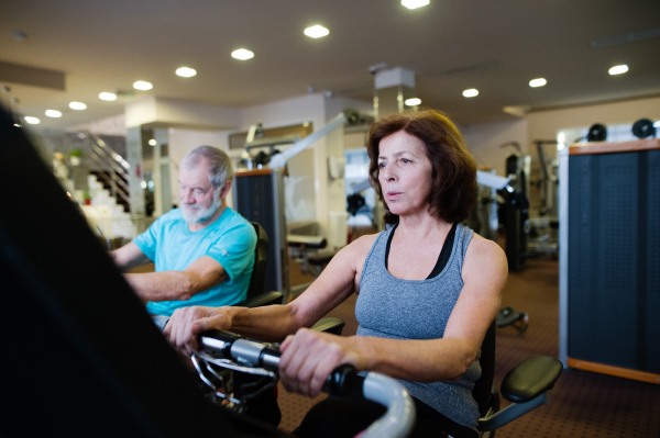 Beautiful fit senior couple in sports clothing in gym doing cardio workout, exercising on recumbent bicycle. Sport fitness and healthy lifestyle concept.