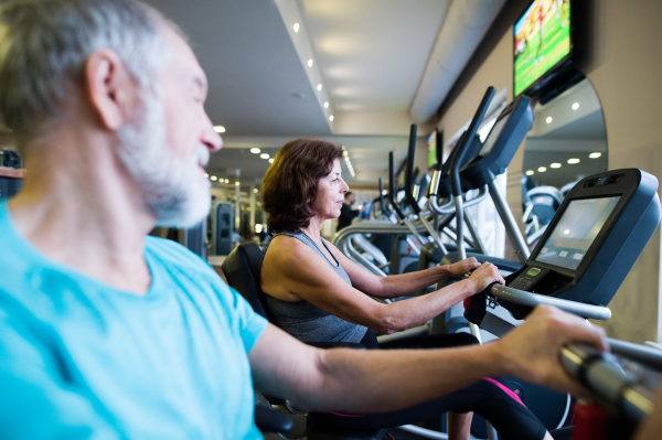 Beautiful fit senior couple in sports clothing in gym doing cardio workout, exercising on recumbent bicycle. Sport fitness and healthy lifestyle concept.