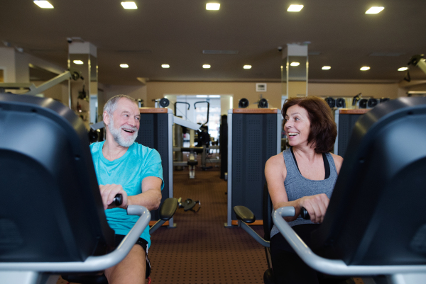 Beautiful fit senior couple in sports clothing in gym doing cardio workout, exercising on recumbent bicycle. Sport fitness and healthy lifestyle concept.