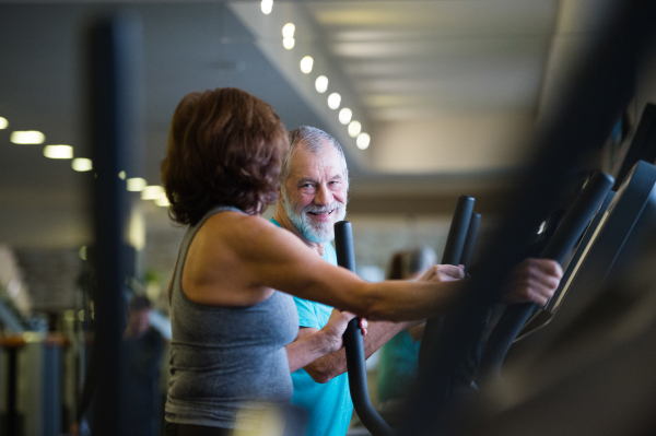 Beautiful fit senior couple in sports clothing in gym doing cardio workout, exercising on elliptical trainer machine. Sport fitness and healthy lifestyle concept.