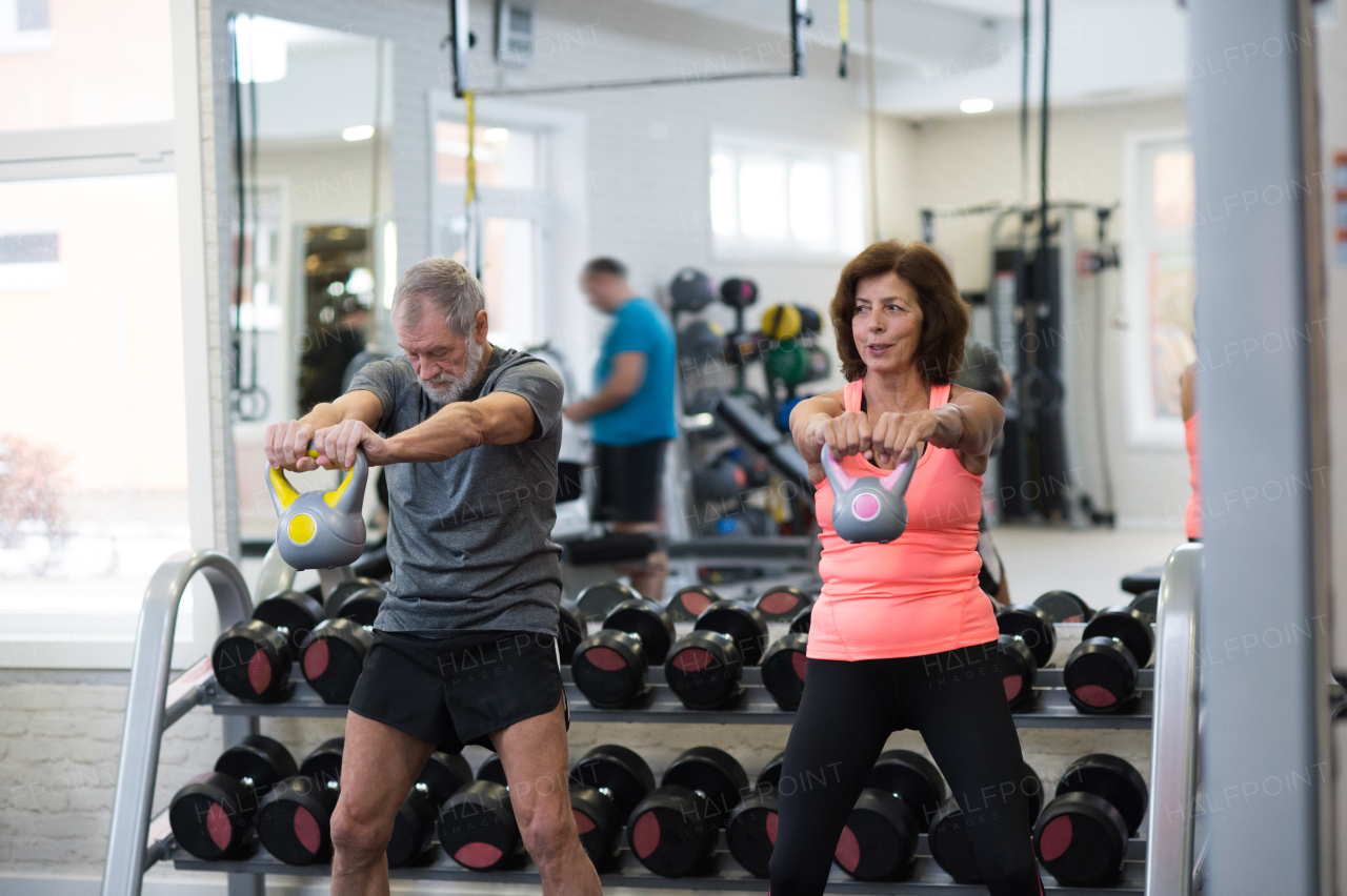 Beautiful fit senior couple in gym working out using kettlebells.