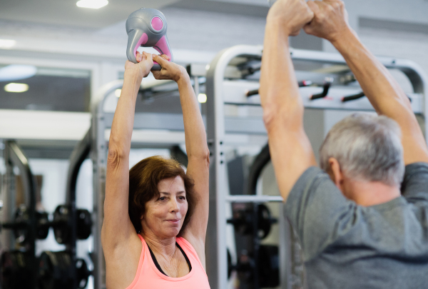 Beautiful fit senior couple in gym working out using kettlebells.