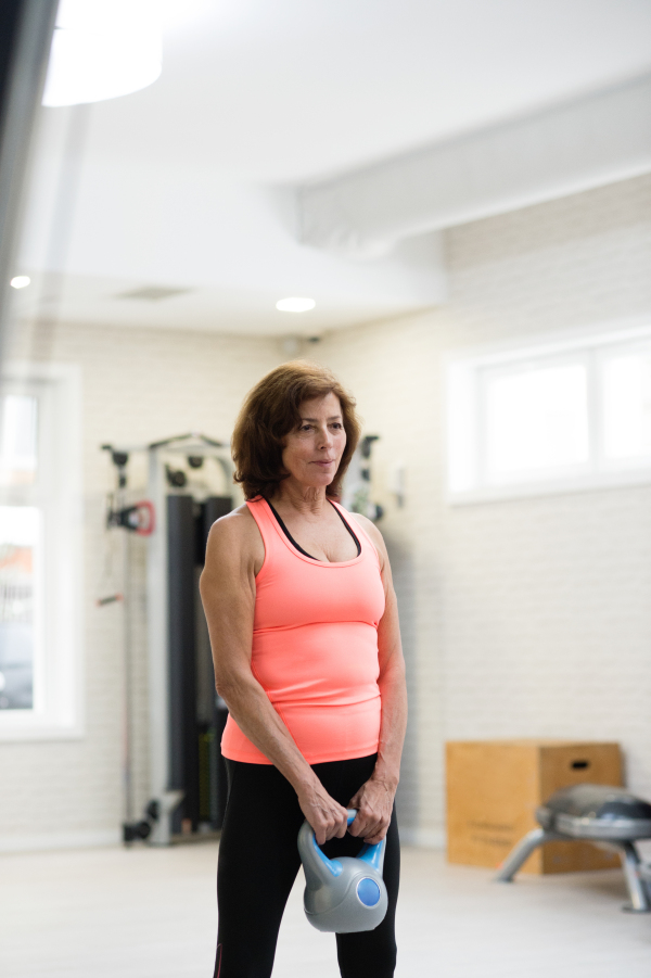 Beautiful fit senior woman in gym working out using kettlebells. Sport, fitness and healthy lifestyle concept.