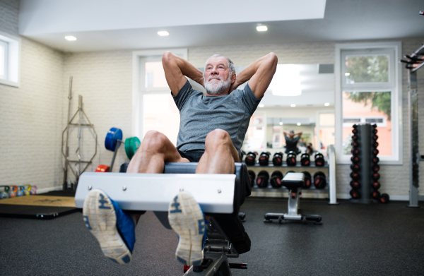 Fit senior man on a bench in gym in sports clothing working his abs, doing abdominal crunches.