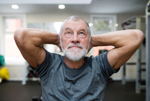 Fit senior man in gym in sports clothing working his abs, doing abdominal crunches.