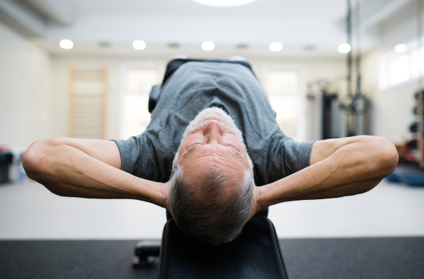 Fit senior man lying on a bench in gym in sports clothing working his abs, doing abdominal crunches.