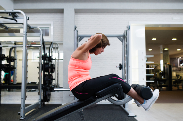 Beautiful fit senior woman in gym in sports clothing working her abs, doing abdominal crunches.