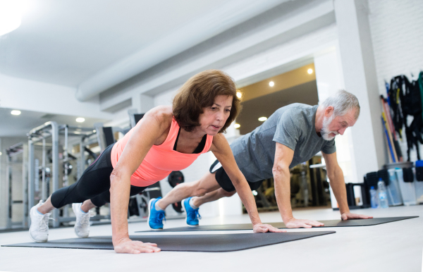 Beautiful fit senior couple in gym working out, doing push ups.