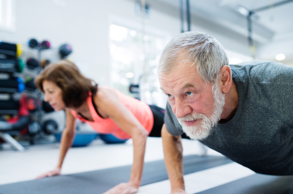 Beautiful fit senior couple in gym working out, doing push ups.