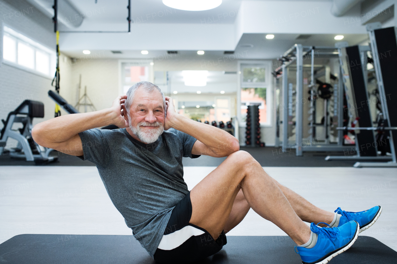 Fit senior man in gym in sports clothing working his abs, doing abdominal crunches.