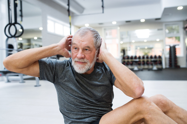 Fit senior man in gym in sports clothing working his abs, doing abdominal crunches.