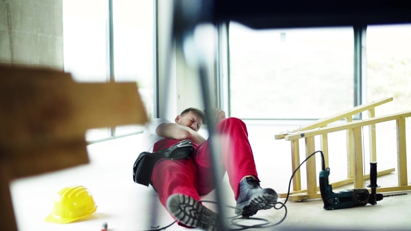 Accident of a male worker at the construction site. An injured man sitting on the floor. Slow motion.