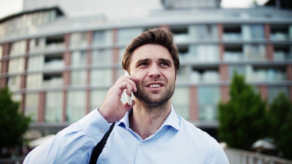 A young businessman with a smartphone walking on a bridge, making a phone call. Slow motion.