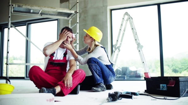 Accident of a male worker at the construction site. A woman helping her injured colleague, wiping his forehead. Slow motion.