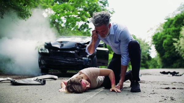 A man helping a young injured woman lying on the road after a car accident, making a phone call. Slow motion.