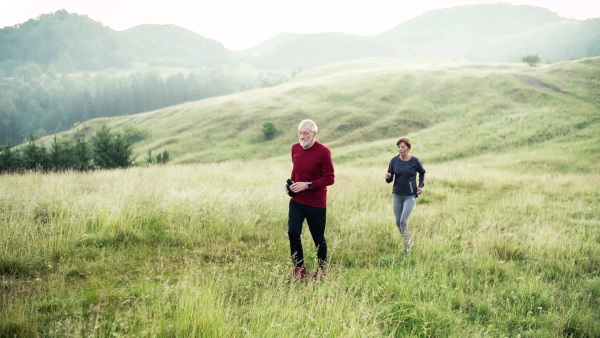 Senior sporty couple running on meadow outdoors in sunny nature in the foggy morning. Slow motion.