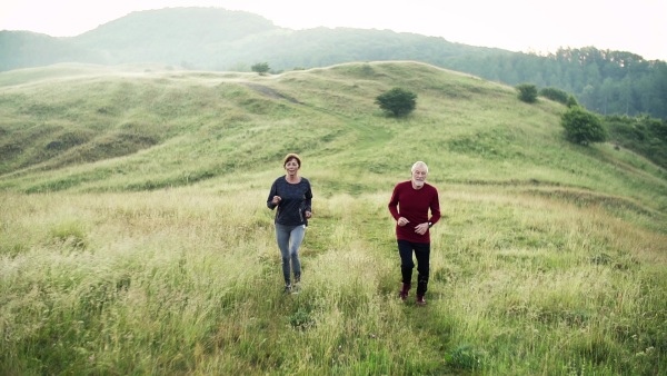 Senior sporty couple running on meadow outdoors in sunny nature in the foggy morning. Slow motion.