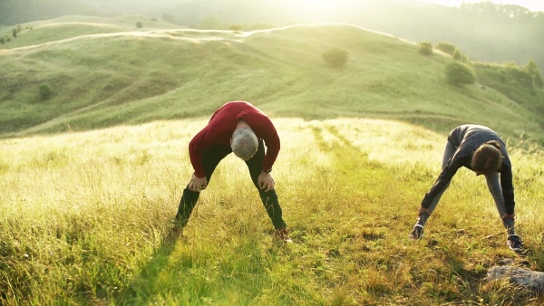 Senior couple runners stretching on meadow outdoors at sunrise in nature. Slow motion.