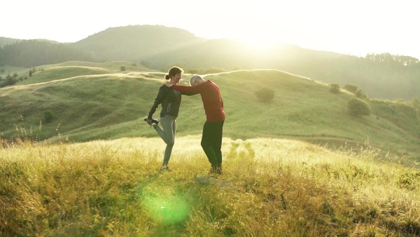 Senior couple runners stretching on meadow outdoors at sunrise in nature. Slow motion.