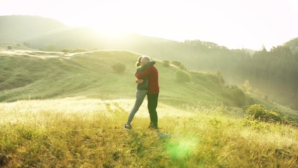 Senior couple runners hugging on meadow outdoors at sunrise in nature. Slow motion.