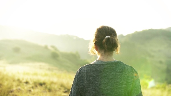 Senior woman runner walking on meadow outdoors at sunrise in nature, encouraging someone to come to her. Slow motion.