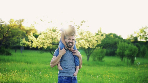 Father giving small daughter a piggyback ride in spring nature at sunset. Slow motion. Copy space.