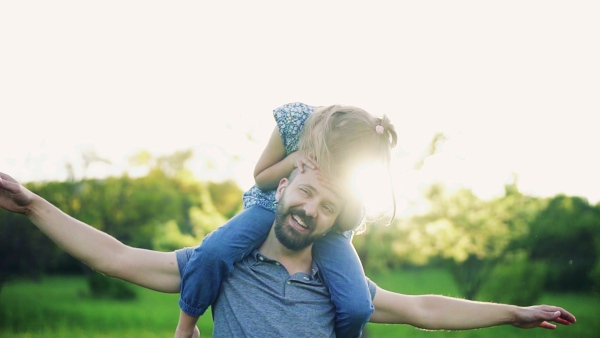 Father giving small daughter a piggyback ride in spring nature at sunset, having fun. Slow motion.