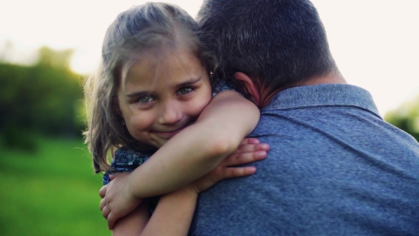 Unrecognizable father holding a small daughter in sunny spring nature, having fun . Slow motion.