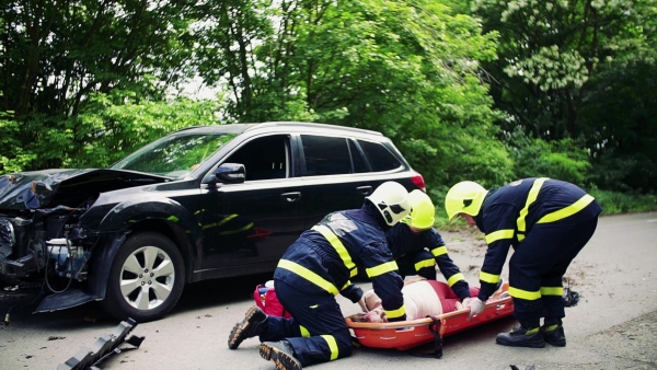 Firefighters putting a young injured woman into a plastic stretcher on the road after a car accident. Slow motion.