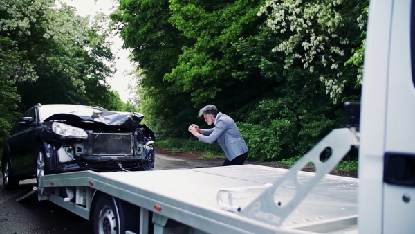 Mature man in gray suit taking pictures of a broken car after an accident. Tow truck service concept. Slow motion.