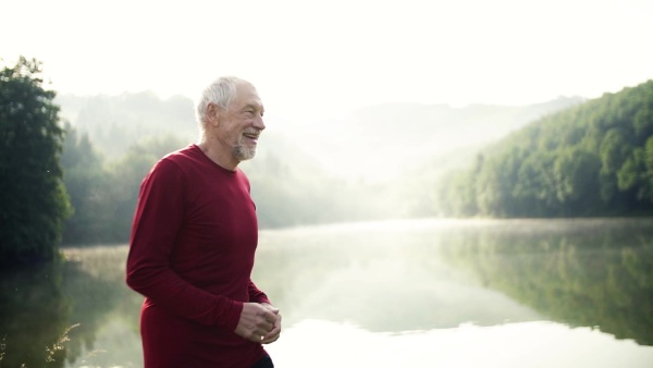 Senior man runner jogging by the lake outdoor in foggy morning in nature. Slow motion.