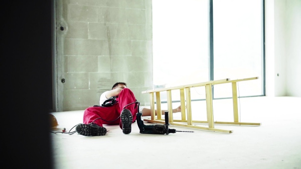 Accident of a male worker at the construction site. An injured man sitting on the floor. Slow motion.