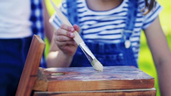 Unrecognizable father with a small daughter outside, painting. Wooden birdhouse or bird feeder making. Slow motion.