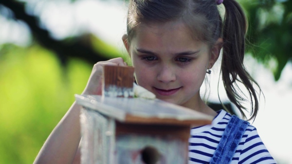 A small girl outside, painting a wooden birdhouse or bird feeder. Slow motion.