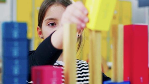 A small girl with teacher sitting at the desk at school, learning.