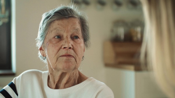 Portrait of an elderly grandmother with an unrecognizable adult daughter or granddaughter talking at home.