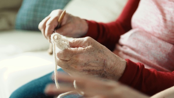 Hands of unrecognizable elderly grandmother and adult granddaughter at home, knitting and unweaving.