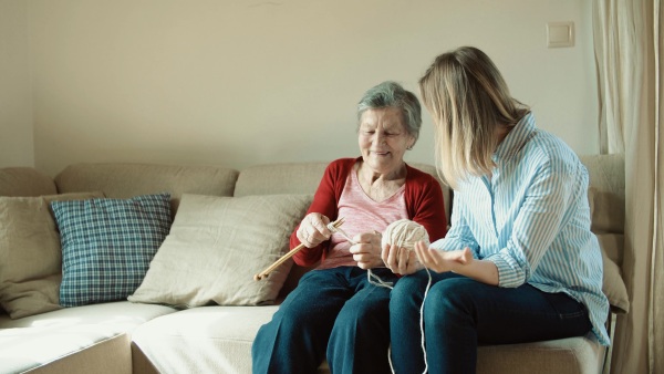 An elderly grandmother and adult granddaughter at home, knitting.