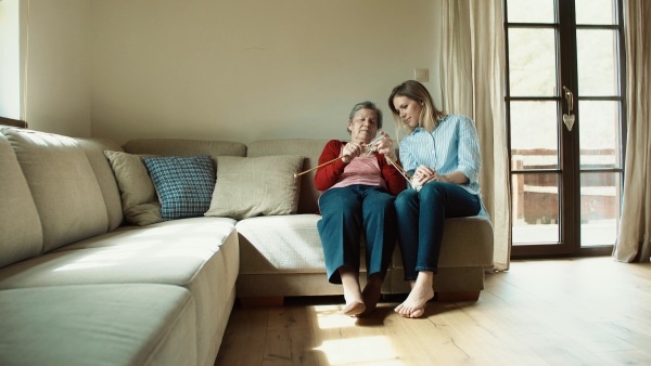 An elderly grandmother and adult granddaughter at home, knitting.