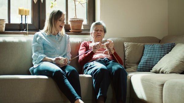 An elderly grandmother and adult granddaughter at home, knitting and talking.